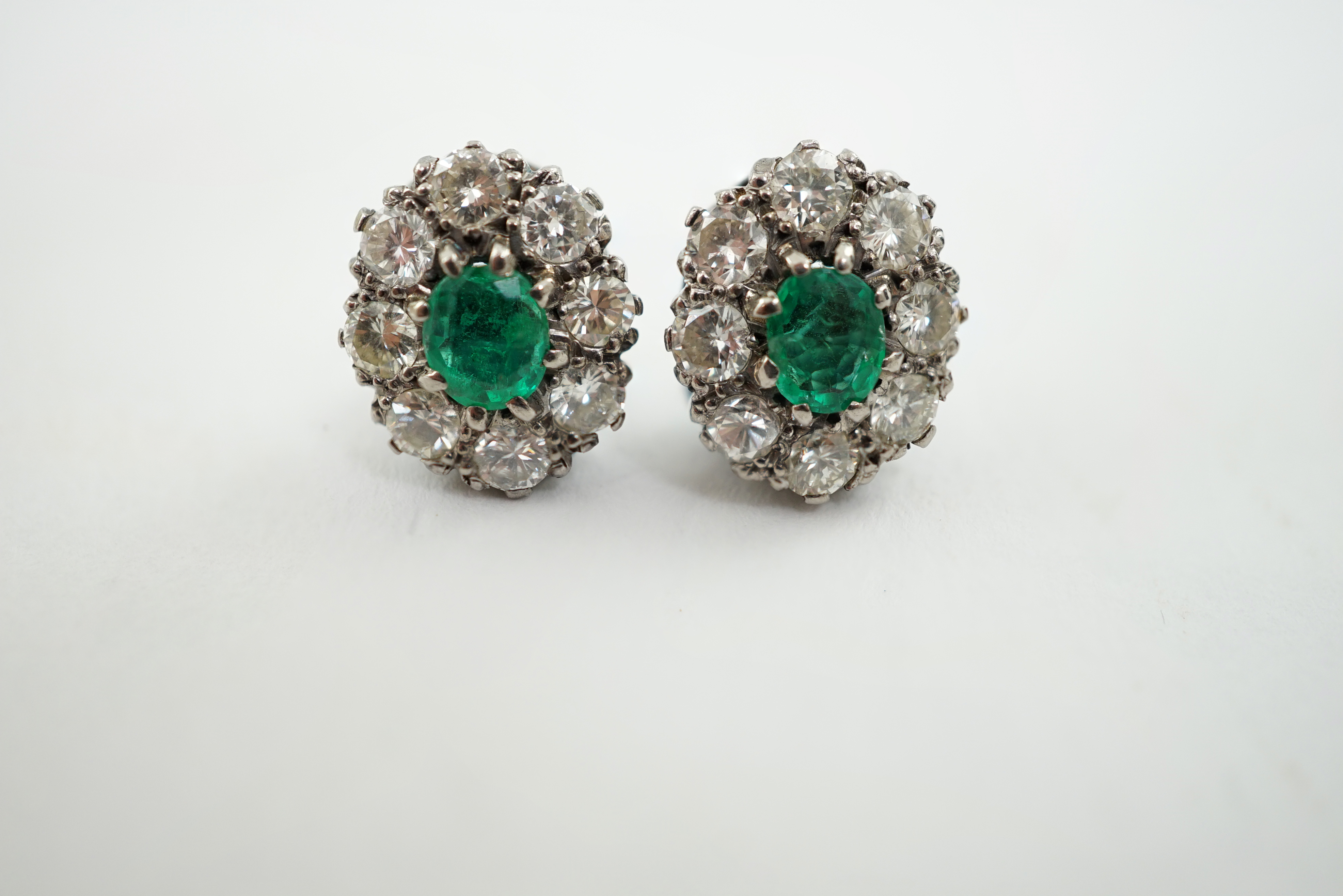 A pair of white gold, single stone emerald and eight stone diamond set oval cluster earrings